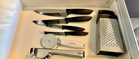 A drawer containing various kitchen utensils including knives, a grater, a spatula, and a grater box.
