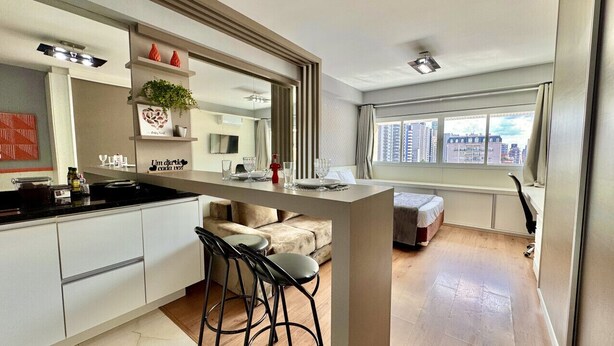 Une chambre d’hôtel moderne dotée d’un coin cuisine, d’une table à manger avec des chaises, d’un canapé et d’une grande fenêtre donnant sur la ville.