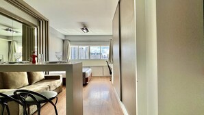 Une chambre d’hôtel moderne équipée d’un canapé, d’une table à manger, de chaises et d’une grande fenêtre donnant sur la ville.
