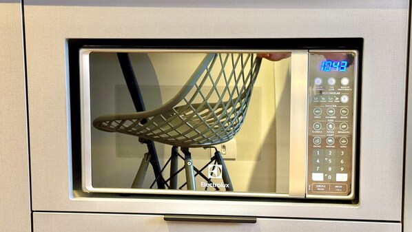 Een magnetron met een digitaal display dat de tijd 10:43 aangeeft, een bedieningspaneel met diverse knoppen, en een stoel die in de deur van de magnetron wordt weergegeven.