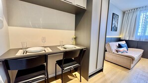 A compact living space with a dining area featuring a table set for two, a sofa, and a window with curtains.