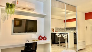 A modern living room with a flat-screen TV, a white sofa, and a small table with decorative items.