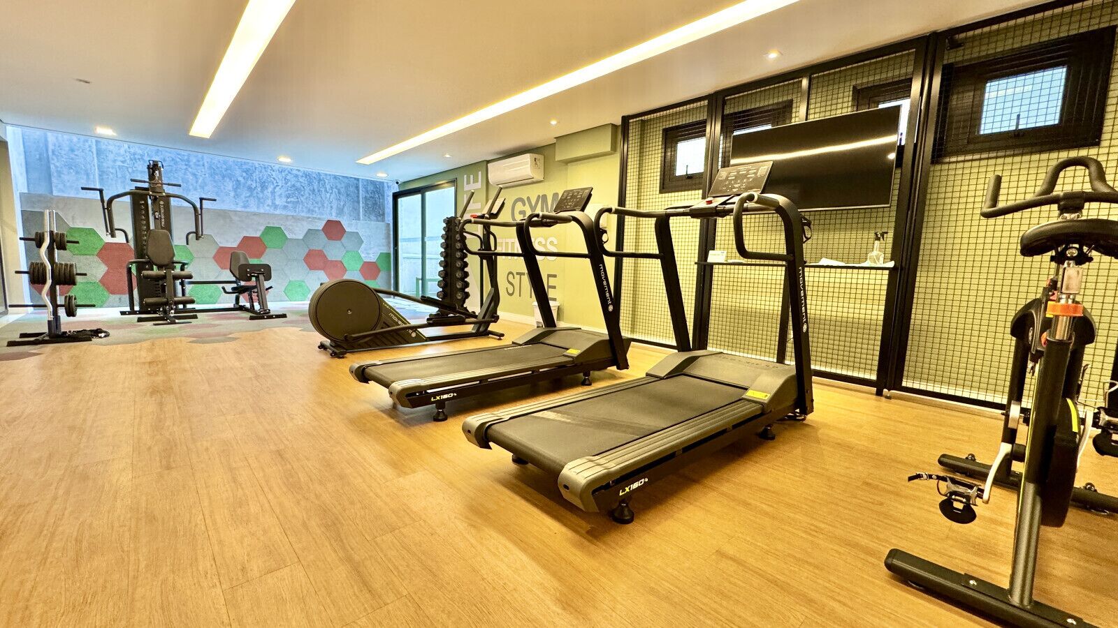 Un gimnasio con cintas de correr, máquinas de pesas y piso de madera.