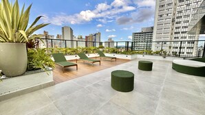 A rooftop terrace with lounge chairs, round ottomans, and potted plants. - Studio compacto próximo CoutoPereira com Ar e vaga (Curitiba)