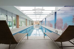 An indoor swimming pool with two lounge chairs, a clear view of the pool, and a mural of coral reefs on the right wall. - 1 Quarto, Espaçoso para até 4 pessoas no Lifespace (Curitiba)