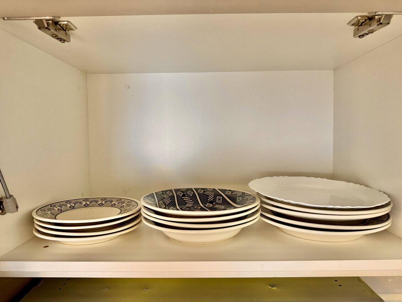 A shelf with three stacked plates, two with a black and white pattern and one plain white.