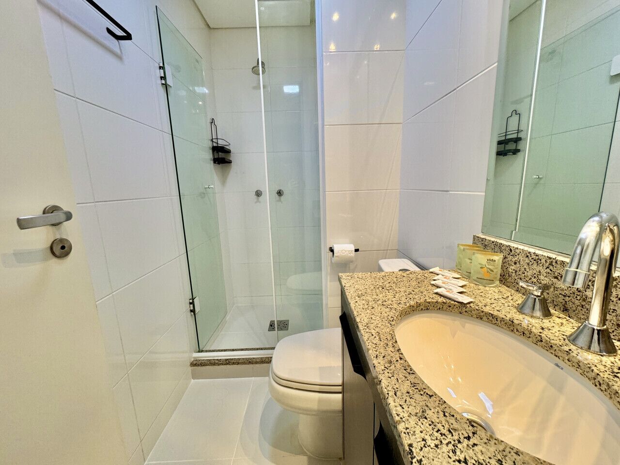 Un baño moderno con cabina de ducha de vidrio, inodoro blanco y lavamanos de granito con grifo cromado.