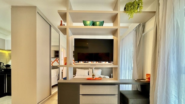 Una habitación de hotel moderna con una isla central, una cama con ropa de cama blanca, un televisor en la pared y una escalera que conduce a un nivel superior.