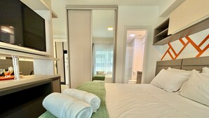 Habitación de hotel con cama, escritorio y televisor de pantalla plana, y baño visible a través de una puerta de vidrio.