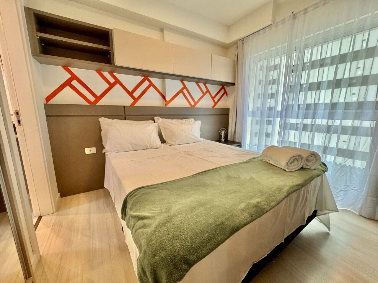A hotel room with a bed, a green blanket, and a window with curtains.