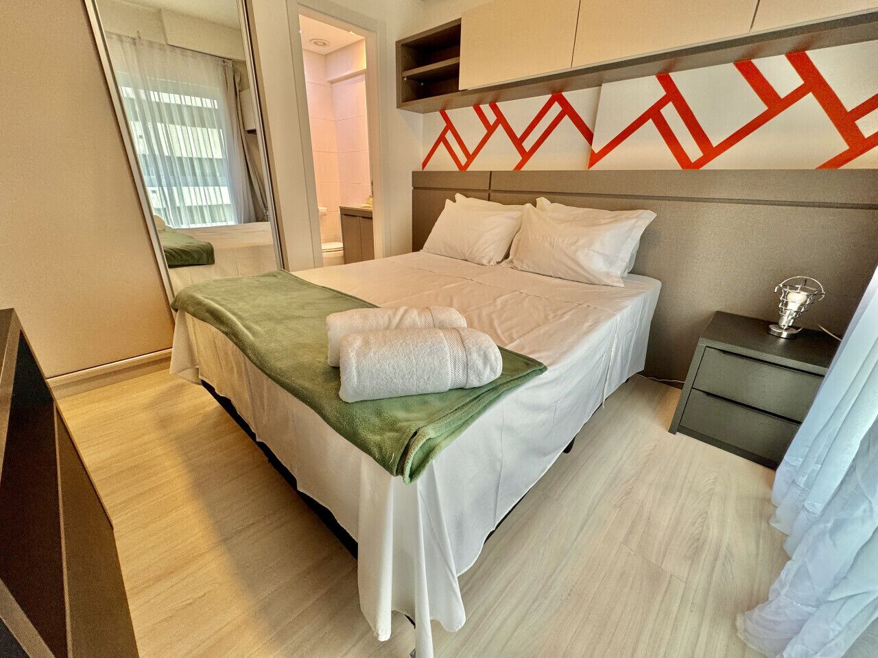 A hotel room with a bed, a nightstand, a mirror, and a geometric wall design.