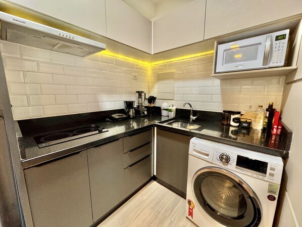 A compact kitchen with a microwave, stove, and washing machine.