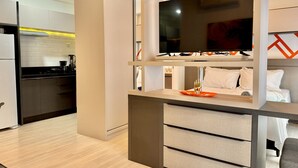 Una cocina moderna con televisor incorporado, un comedor con mesa y sillas, y una sala de estar separada con cama.