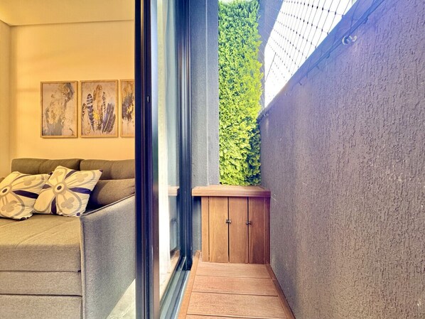 Una sala moderna con un sofá gris, almohadones decorativos y obras de arte en la pared. Se ve un aparador de madera en la esquina, y una pared verde aporta un toque natural.