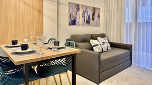 A modern living room with a dining area, featuring a sofa, a dining table set with plates and glasses, and abstract art on the wall.