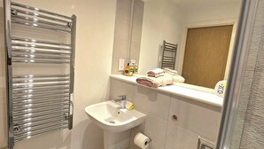 Ein Badezimmer mit chromfarbener Handtuchstange, Waschbecken mit Spiegel darüber und Toilette.