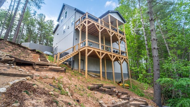 A multi-story wooden house with a balcony, surrounded by a forest.