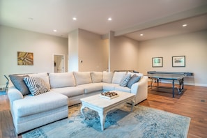 A living room with a sectional sofa, a coffee table, a ping pong table, and a large painting on the wall. - New four bedroom house with private dock on Lake James.  (Nebo)