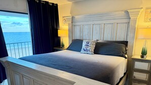 Un dormitorio con una cama grande, vista al mar y una mesita de noche con lámpara.