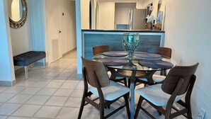Un comedor con una mesa redonda de vidrio, cuatro sillas y un jarrón decorativo de vidrio.