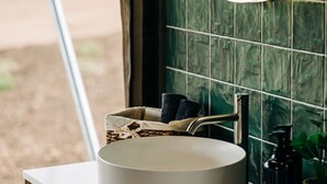 Une salle de bain avec un lavabo rond, un miroir et une vue sur la verdure à l’extérieur.