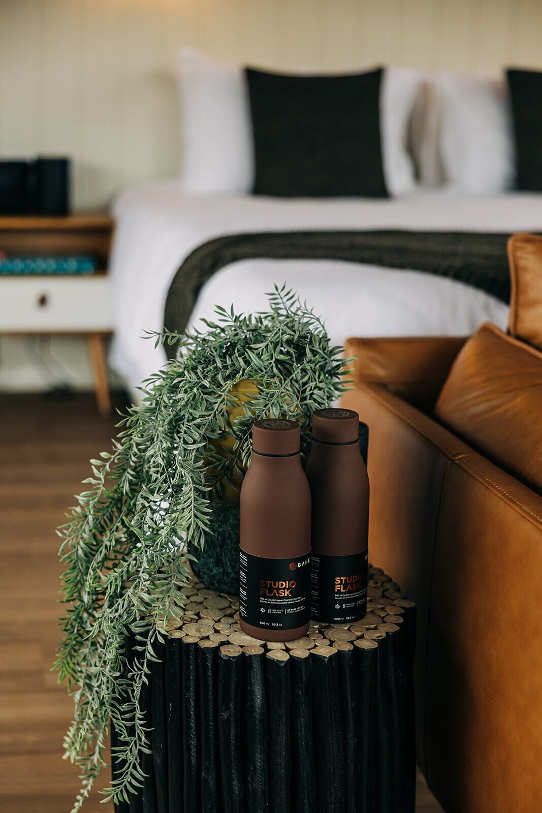 A bedroom with a bed, a nightstand, and a coffee table with two Studio Flask bottles and a decorative plant.
