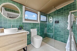 A bathroom with green tiles, a round mirror, a toilet, and a sink with a wooden cabinet.