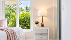 A bedroom with a bed, a nightstand with a lamp, and a window with a view of greenery. - Dream Gateway, Luxury, Exclusive (Bradenton)