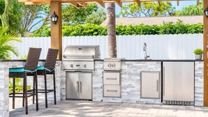 An outdoor kitchen with a grill, refrigerator, and bar stools. - Dream Gateway, Luxury, Exclusive (Bradenton)