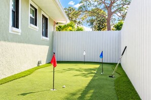 Un jardin avec une pelouse artificielle, un drapeau rouge, un drapeau bleu et un club de golf.