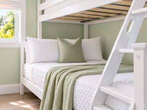 Un lit superposé avec une literie blanche et un plaid vert.
