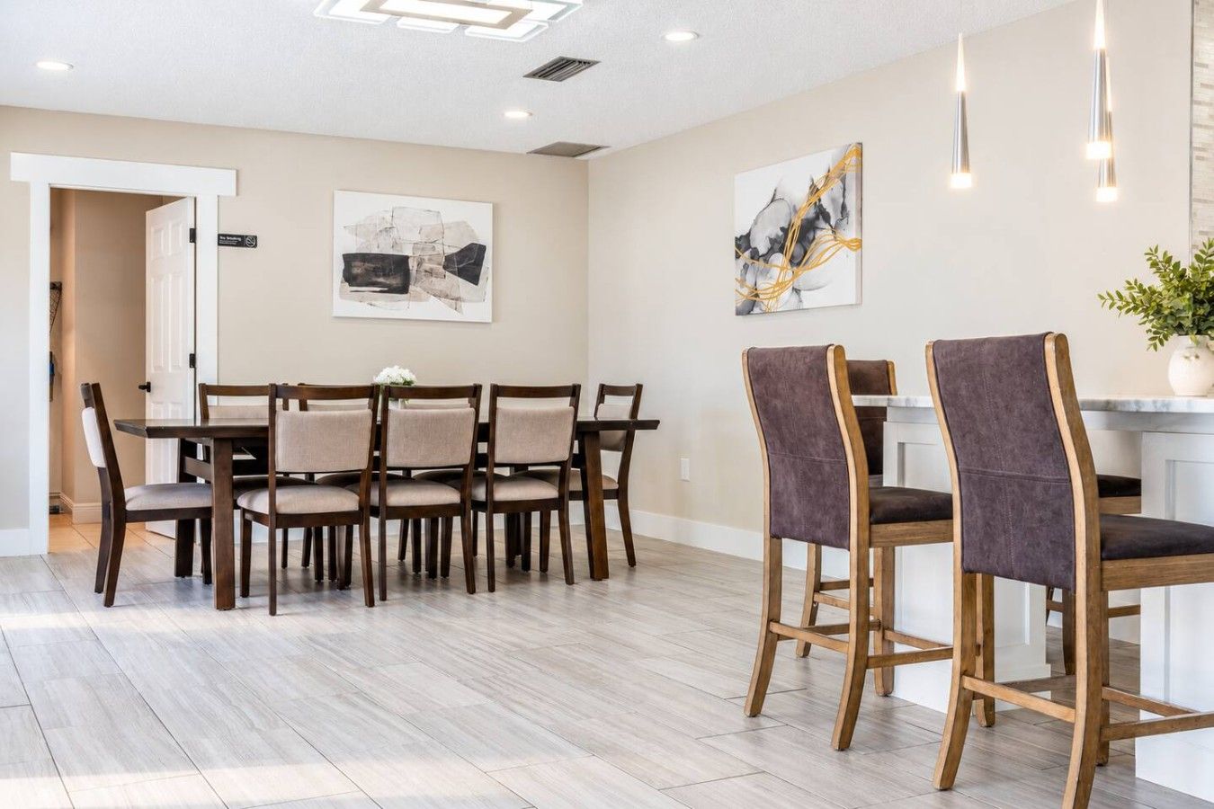 A dining area with a wooden table and chairs, a white door, and two abstract paintings on the wall.