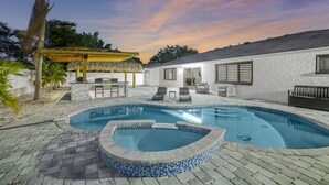 A swimming pool with a tiled edge, a covered seating area, and a building with windows and a door. - Dream Gateway, Luxury, Exclusive (Bradenton)