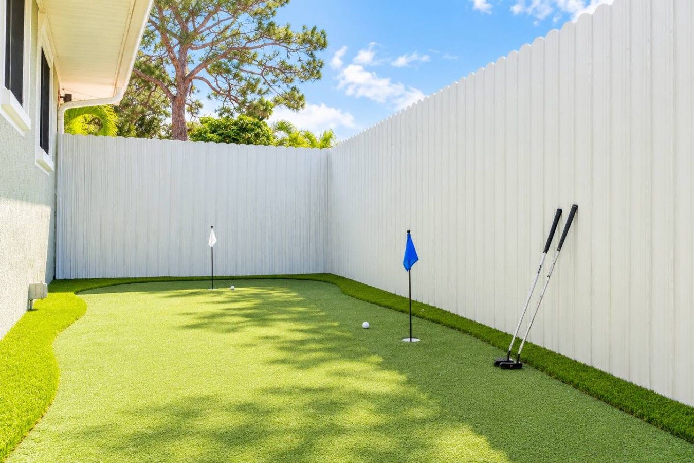 Un jardin avec une pelouse artificielle, une clôture blanche et du matériel de golf.