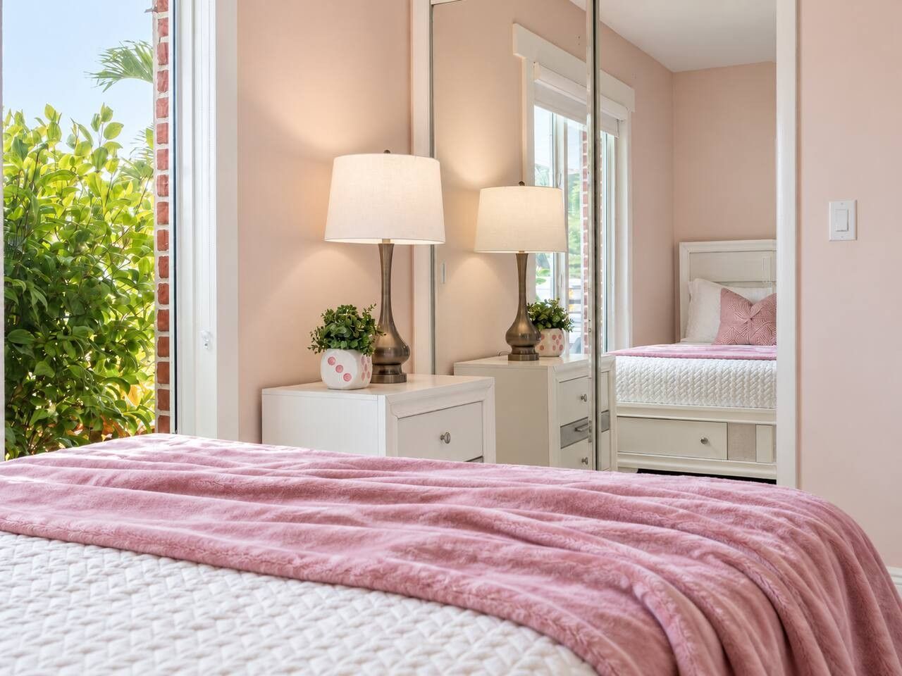 Une chambre à coucher comprenant un lit, deux tables de chevet, un miroir et une fenêtre donnant sur un paysage verdoyant.