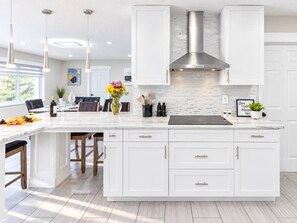 Een moderne keuken met witte kastjes, een groot eiland, hanglampen en uitzicht op de omgeving.