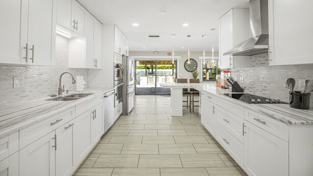 A modern kitchen with white cabinetry, a central island, and a view to the outdoor area. - Dream Gateway, Luxury, Exclusive (Bradenton)