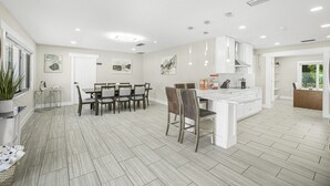 A spacious kitchen with a dining area, featuring a large island, white cabinetry, and a tiled floor. - Dream Gateway, Luxury, Exclusive (Bradenton)