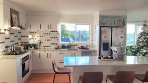 A modern kitchen with white cabinets, a central island with bar stools, a large window, and a refrigerator with magnets.