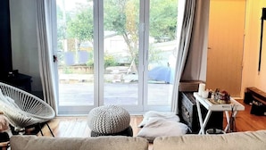 A room with a sofa, a chair, a table with items, and a view through a sliding door.