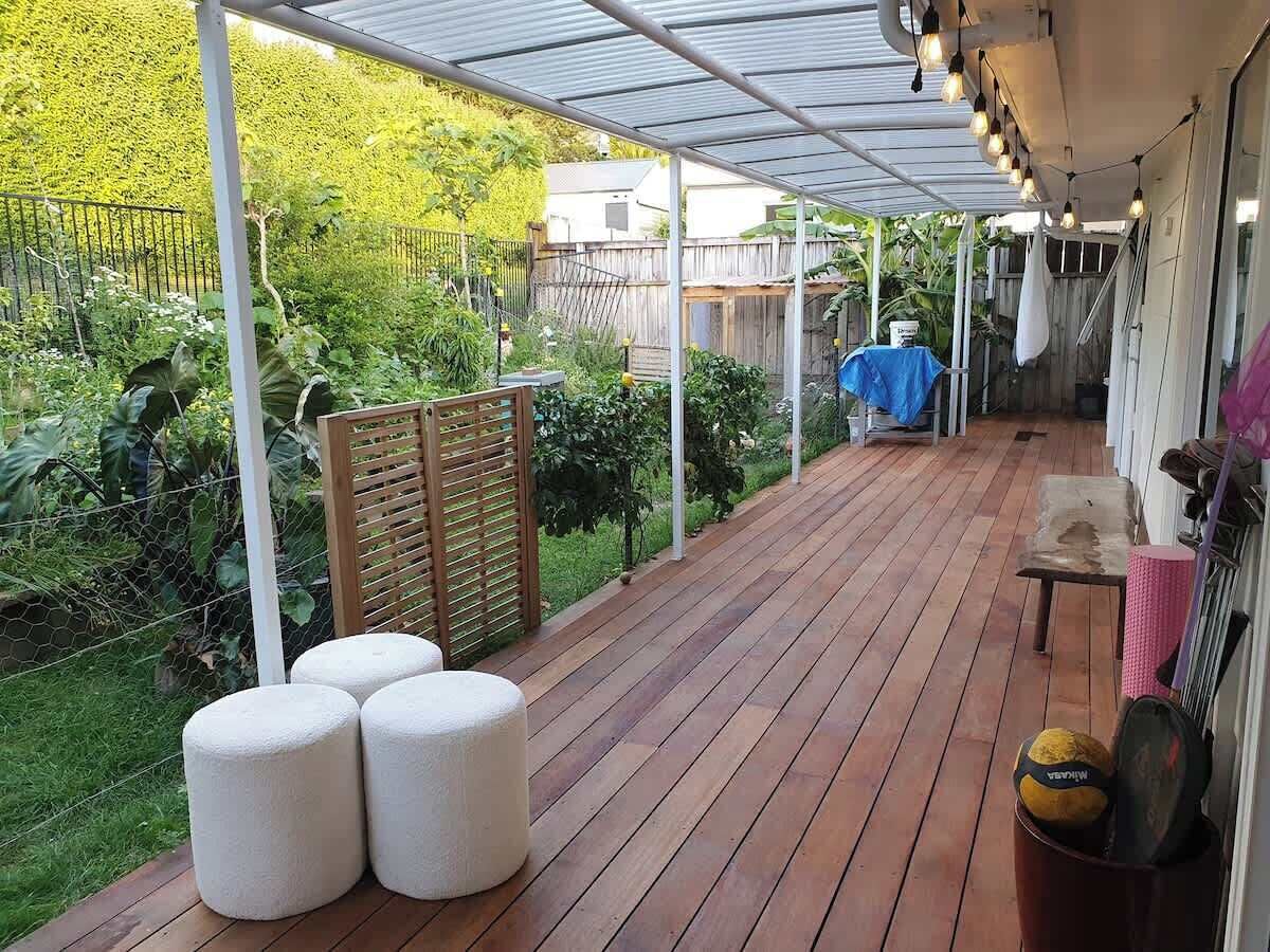 Un patio couvert avec une terrasse en bois, des sièges d’extérieur et un espace jardin.