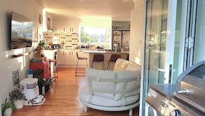 A modern kitchen with white cabinets, a dining area with a white sofa, and a grill outside.