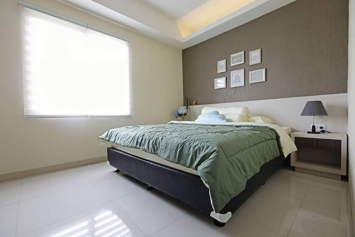 A modern bedroom with a large bed, a bedside table with a lamp, and a window with blinds.