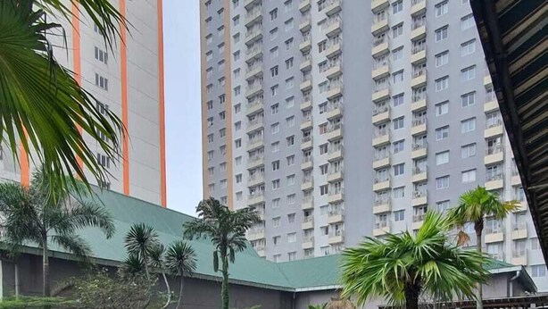 Zona de piscina con sillas de descanso y plantas en macetas, rodeada de edificios residenciales altos.
