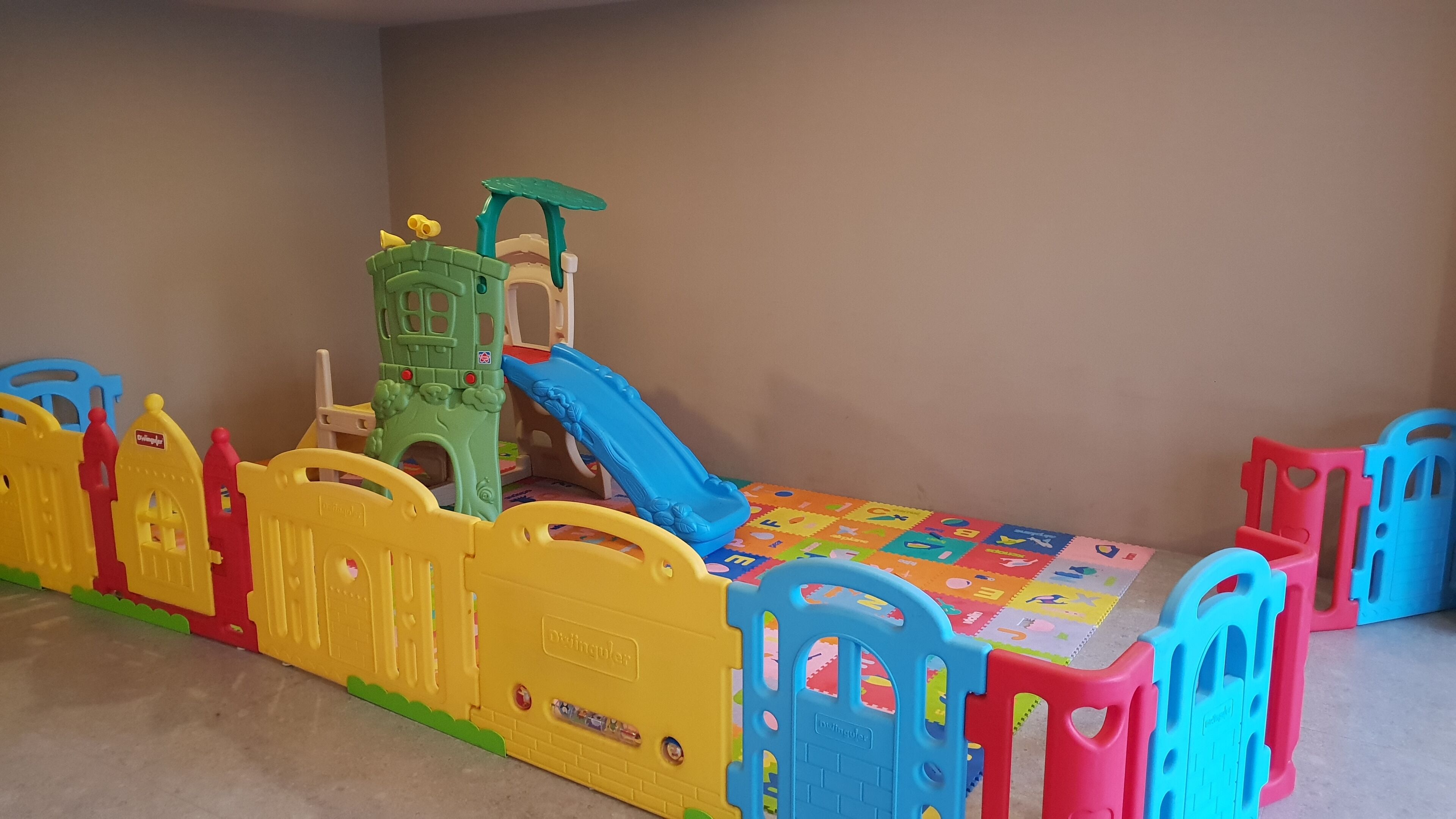 A play area with a slide, play structures, and a colorful foam mat.