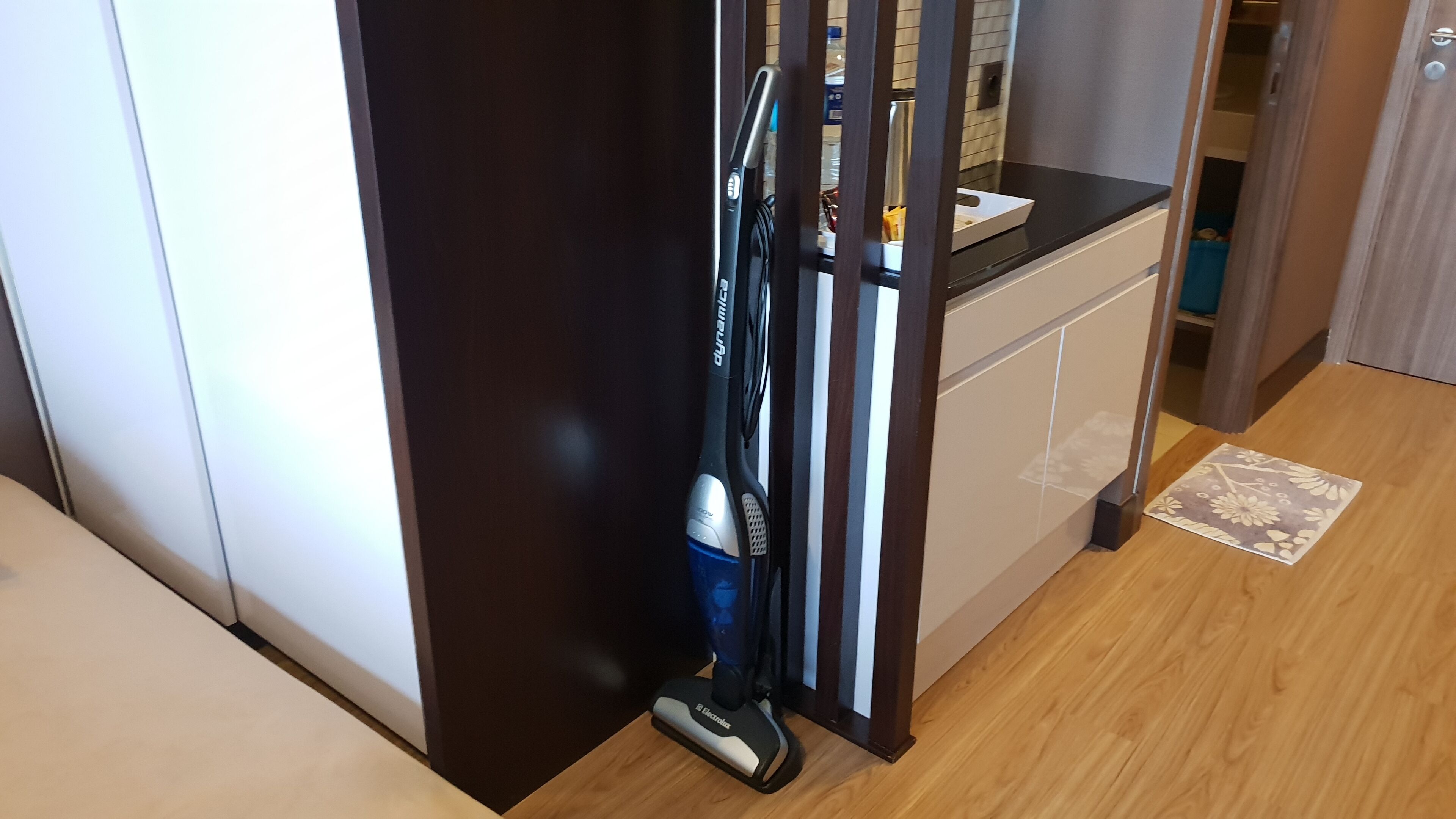 A kitchen with a wooden floor, a black countertop, and a cabinet with a white door.