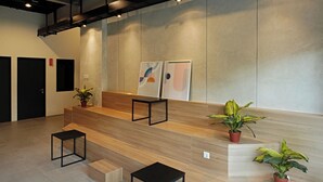 Un área de recepción moderna con un mostrador de madera, mesas de marco negro y plantas en macetas.