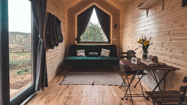 Una habitación acogedora con techo de madera, un sofá verde, una mesita con un florero y una ventana con cortinas.