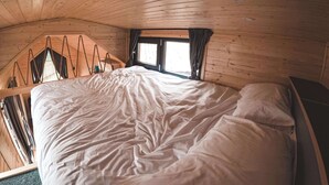 Una habitación de madera con cama, ventana y techo inclinado.