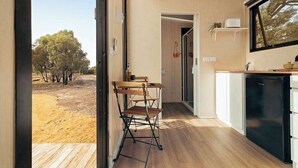 A compact kitchen with a wooden table and chairs, a black refrigerator, and a window overlooking a natural landscape.